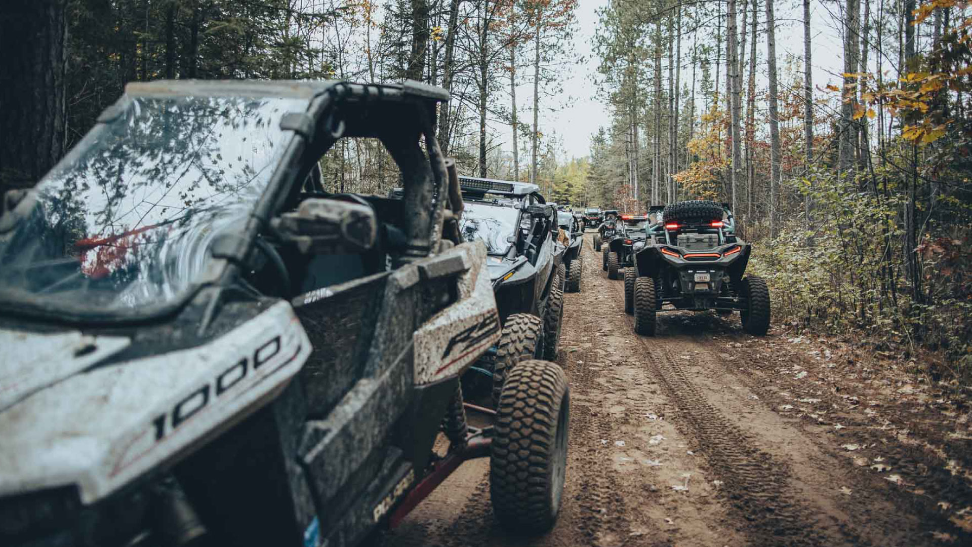 A large group of UTVs lined up on a dirt trail in the woods