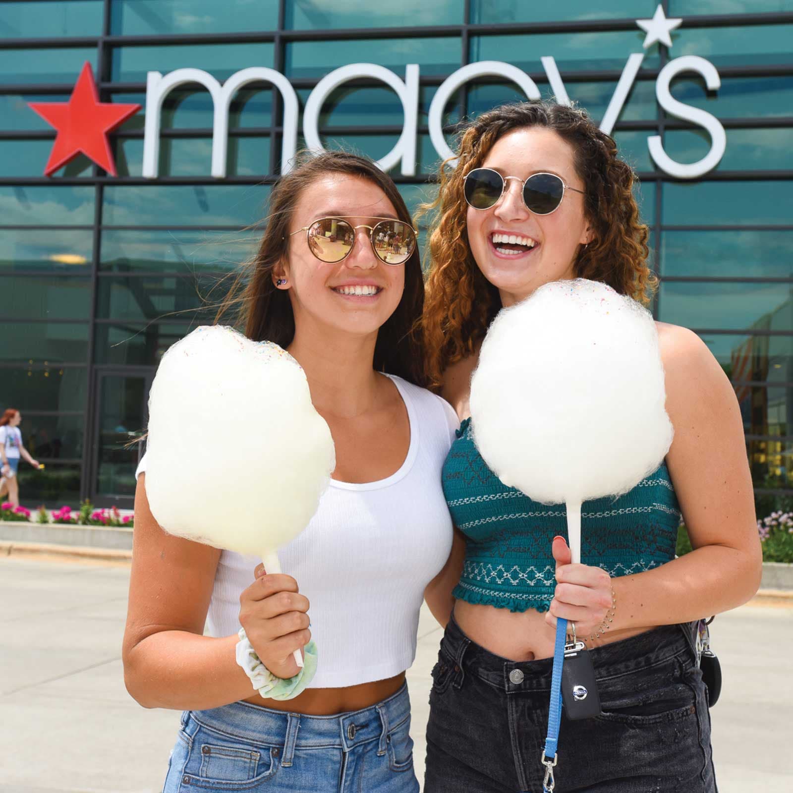 Two women shopping, holding cotton candy in front of Macy's
