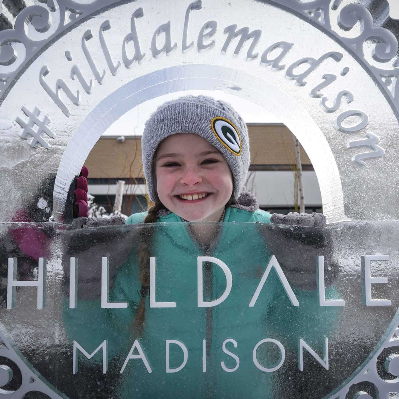 A girl poking her out out of an ice sculpture that says: Hilldale, Madison