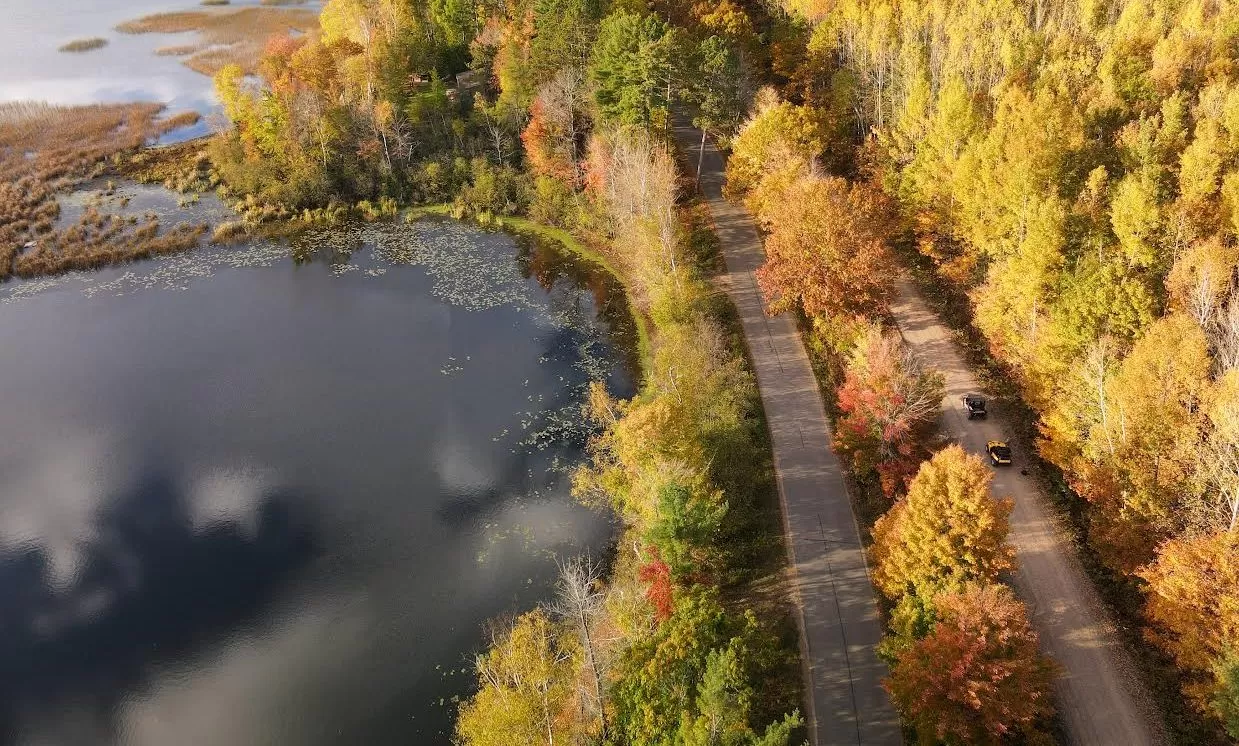 drone photo of UTVers driving on a gravel trail in fall next to water